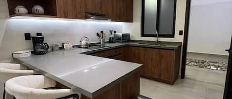 Una cocina moderna con una isla central, taburetes de bar, una cafetera y un bote de basura.