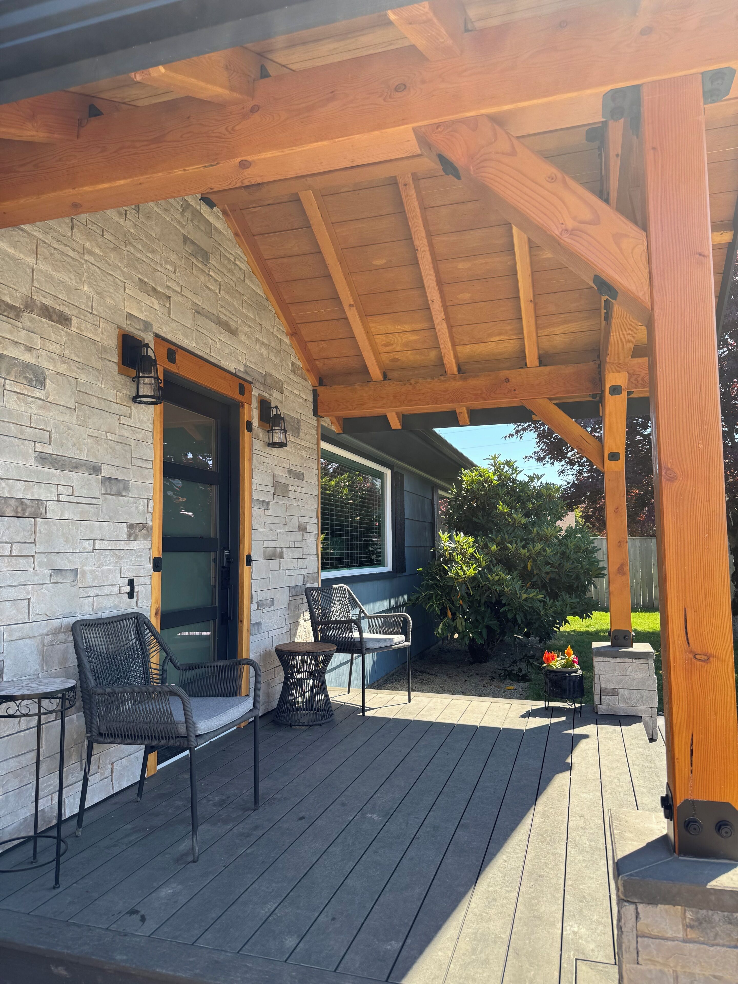 A covered outdoor area with a stone wall, wooden beams, and outdoor furniture.