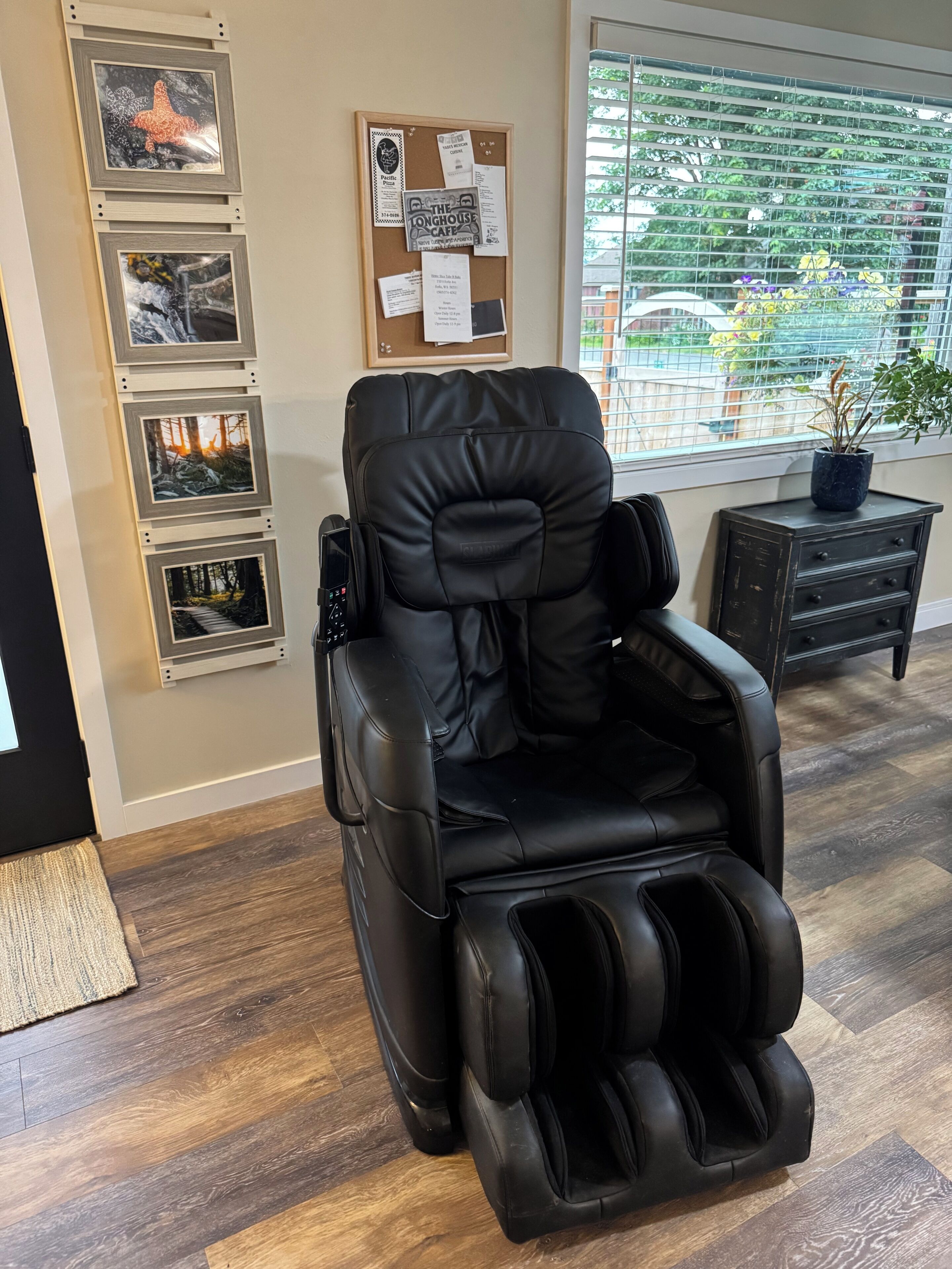 Un fauteuil de massage dans une pièce équipée d’un tableau d’affichage, d’une fenêtre avec des stores et d’une plante en pot.