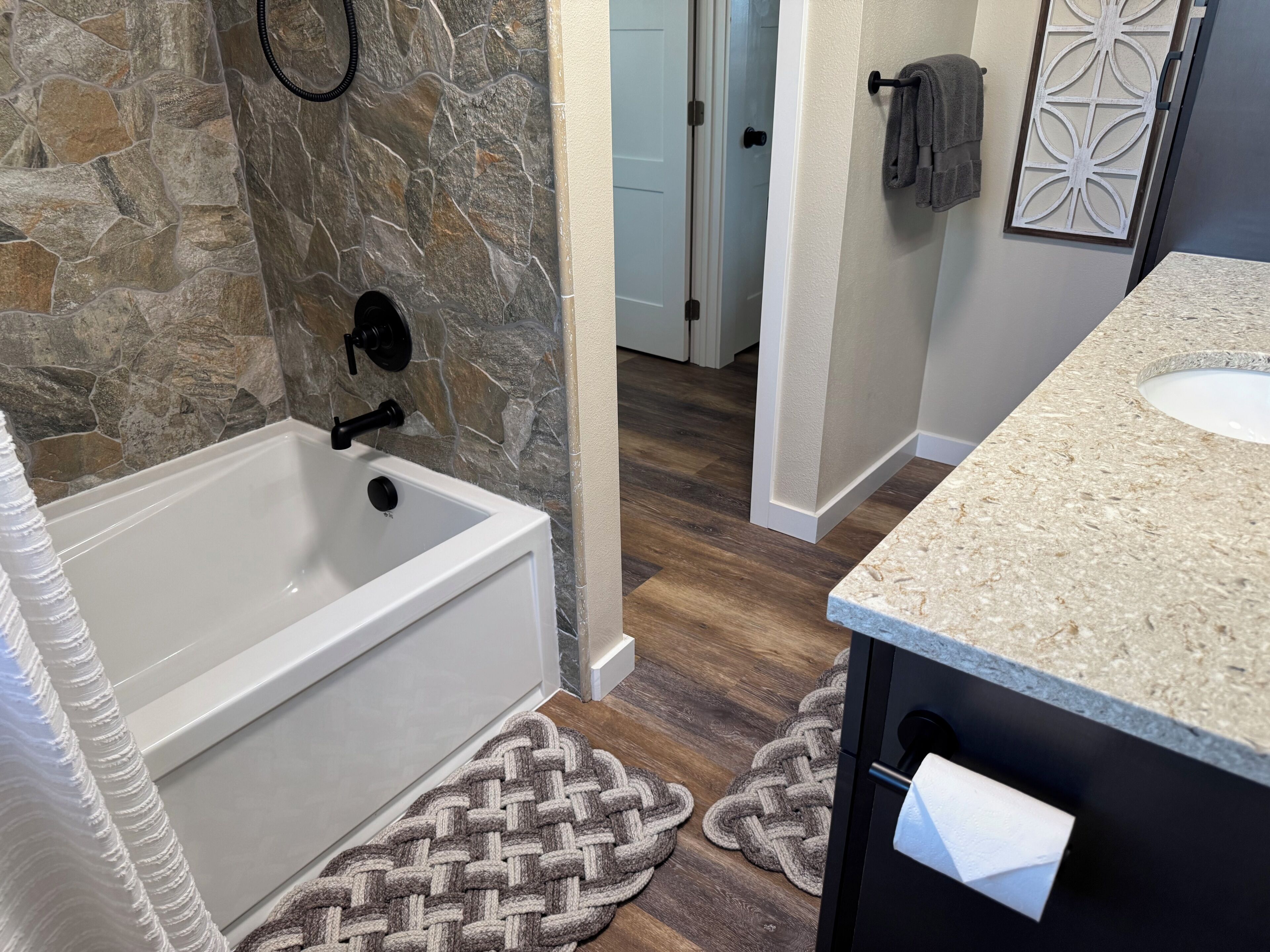 A bathroom with a stone wall, a bathtub, a sink, and a towel rack.