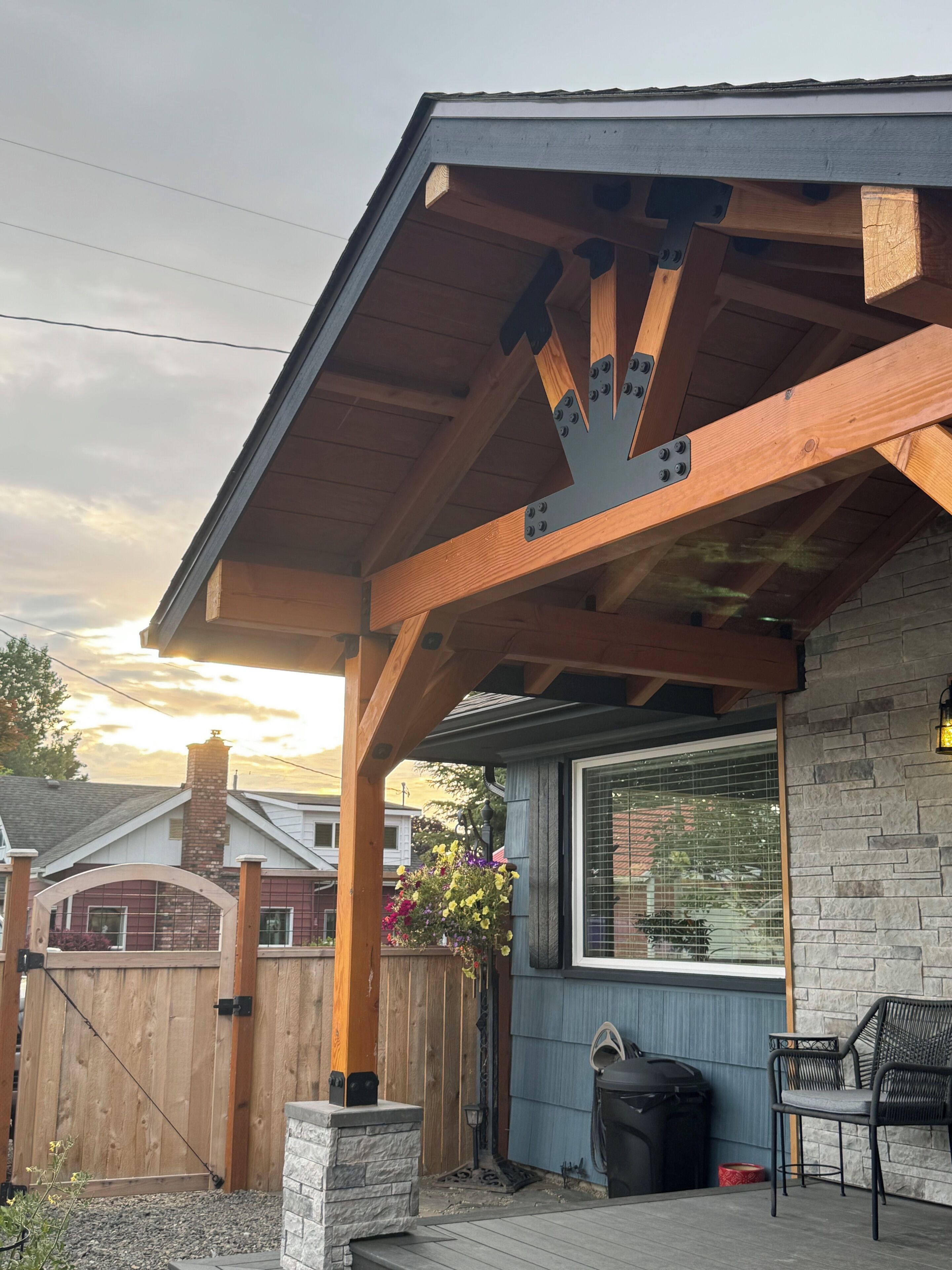 Ein überdachter Patio-Bereich mit Steinmauer, Holzzaun und schwarzem Mülleimer.