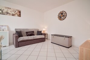 A modern living room with a sofa, a side table, a clock, and a cabinet. - T2 climatisé avec grande terrasse – Plage et Port à pied (Saint-Cyprien)