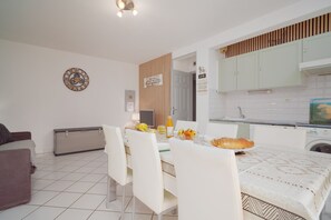 A modern kitchen with white cabinets, a dining area with a table set for two, and a small refrigerator. - T2 climatisé avec grande terrasse – Plage et Port à pied (Saint-Cyprien)