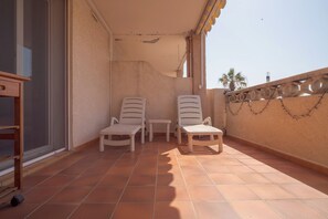 A balcony with two white chairs and a small table, a wooden cabinet, and a tiled floor. - T2 climatisé avec grande terrasse – Plage et Port à pied (Saint-Cyprien)