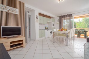 Uma sala moderna com televisão de tela plana, área de jantar com mesa posta para dois e cozinha com máquina de lavar roupa.