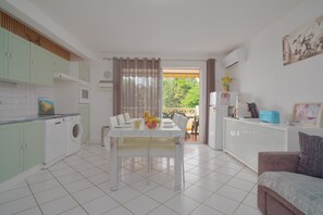 A clean, well-lit kitchen with a dining area, a washing machine, and a view of greenery outside. - T2 climatisé avec grande terrasse – Plage et Port à pied (Saint-Cyprien)
