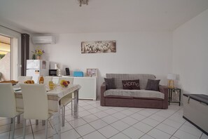 Ein kompakter Wohnbereich mit Essplatz, Küchenzeile und einer Couch mit Zierkissen.