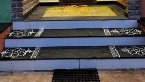 Eine Holztür mit dekorativer Gestaltung, begrenzt von Ziegelstützen, und eine Treppe, die zu ihr hinaufführt.