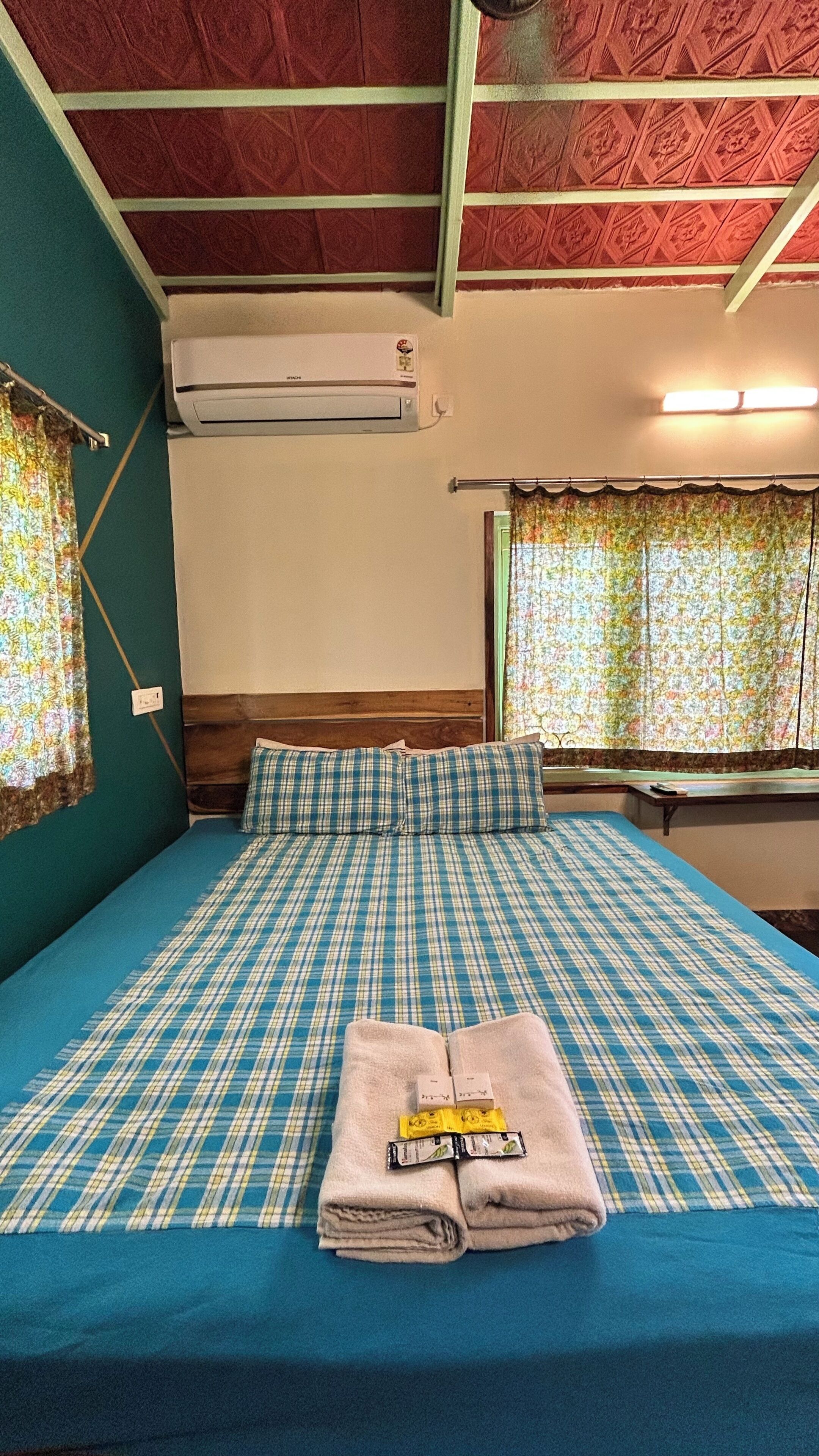 Habitación de hotel con cama, ventana con cortinas, equipo de aire acondicionado y lámpara fijada a la pared.