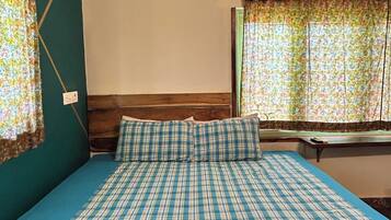 Habitación de hotel con cama, ventana con cortinas, equipo de aire acondicionado y lámpara fijada a la pared.