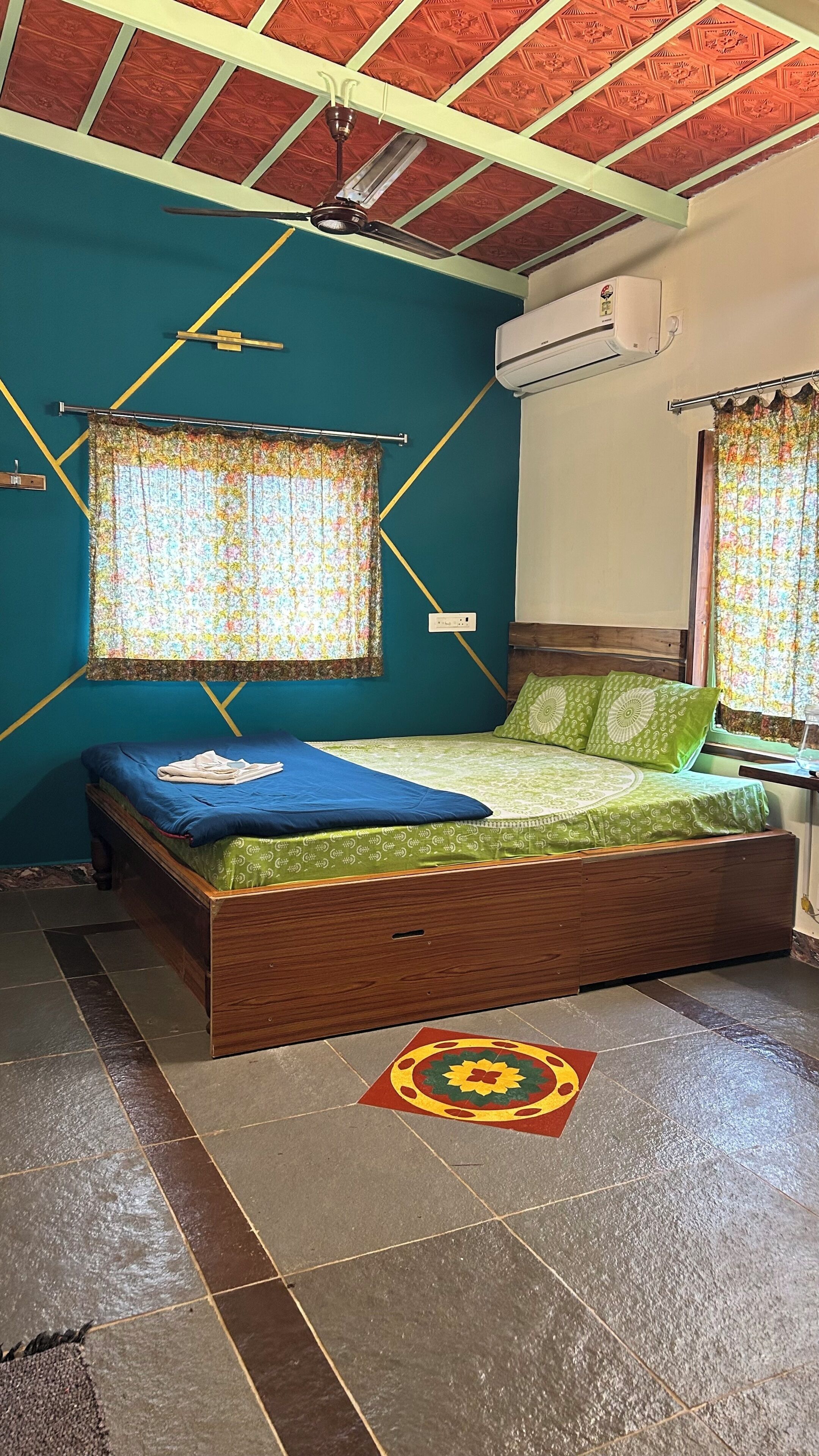 Een kamer met een bed, een raam met gordijnen, een plafondventilator en een airconditioning.