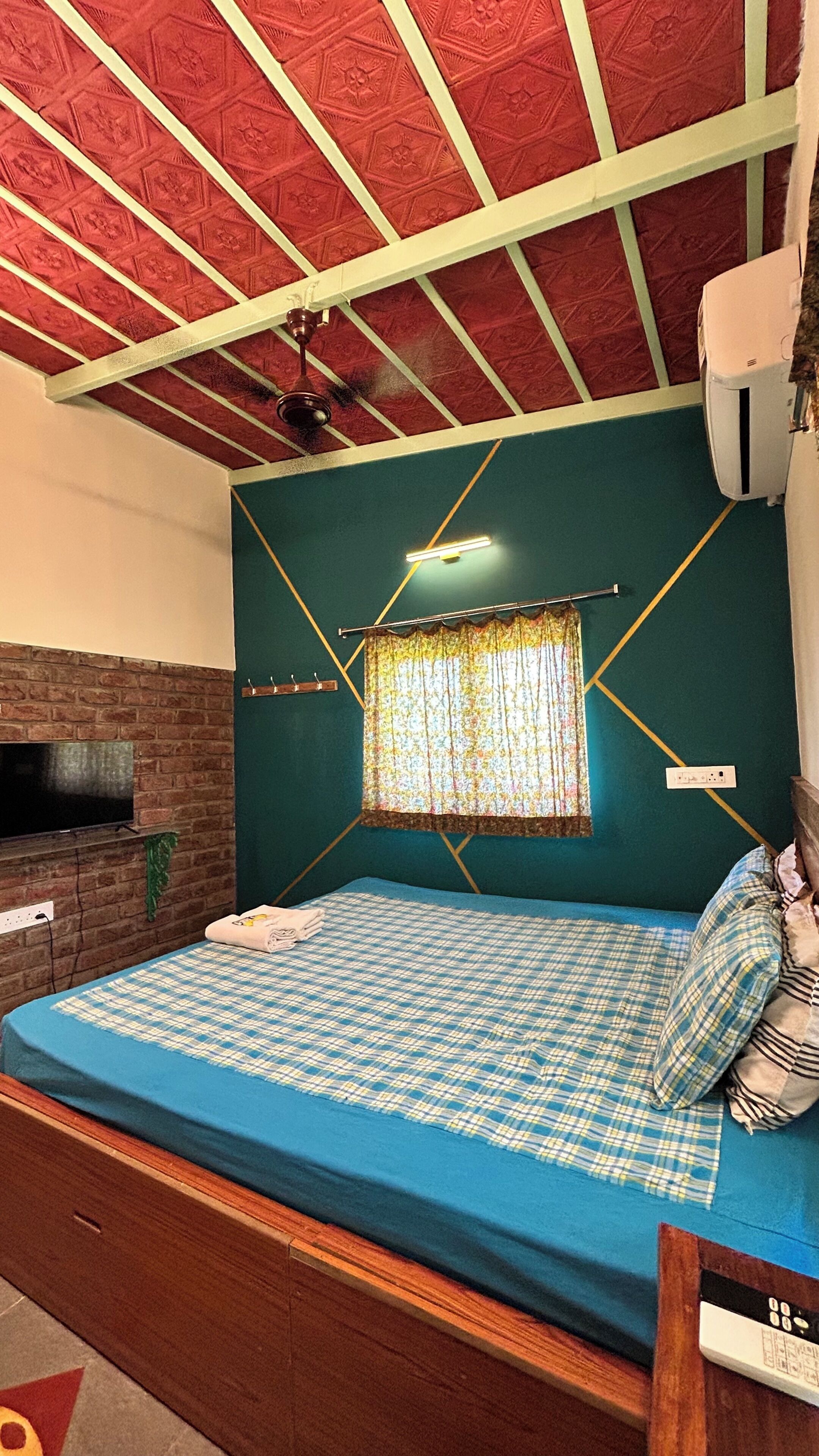Une chambre avec un lit, une télévision, un ventilateur de plafond et une fenêtre avec des rideaux.