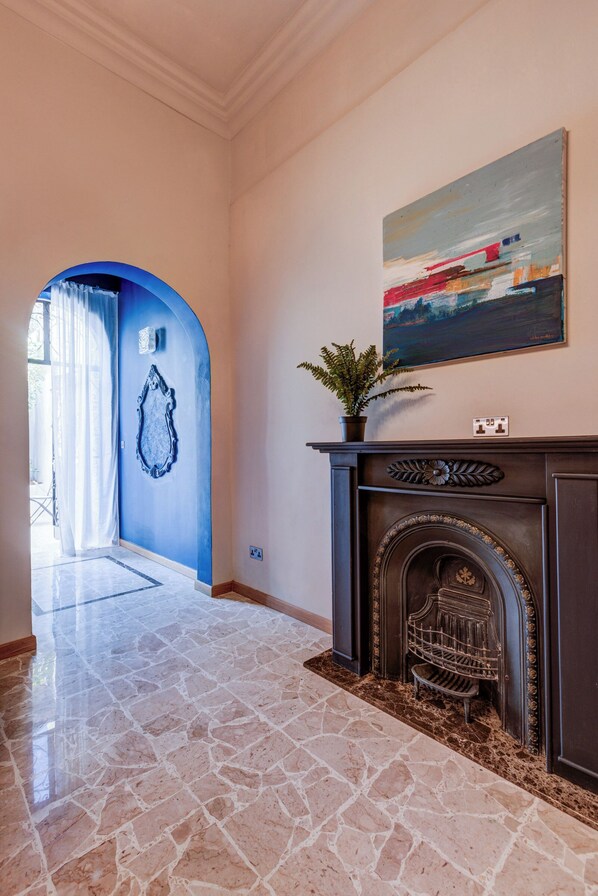 Un couloir avec une arche bleue, une cheminée agrémentée d’une plante et un tableau accroché au mur.