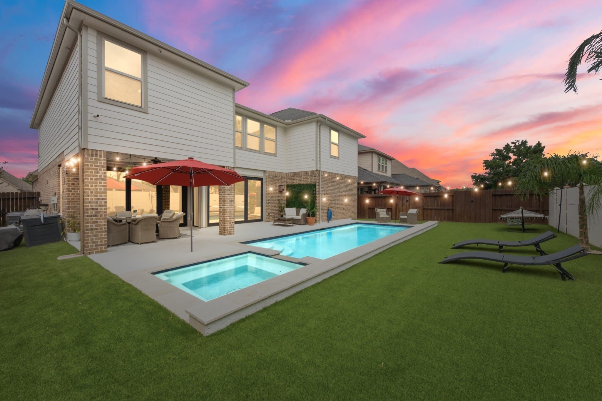 A two-story house with a swimming pool, outdoor seating, and string lights.