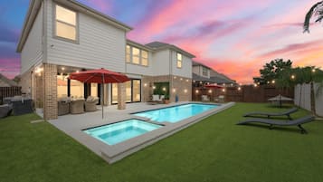 A two-story house with a swimming pool, outdoor seating, and string lights.