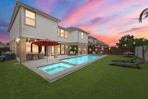 A two-story house with a swimming pool, outdoor seating, and string lights.