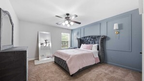 Un dormitorio con cama, ventilador de techo, cómoda, espejo y ventana con persianas.