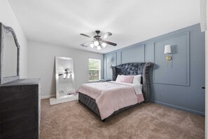 Ein Schlafzimmer mit einem Bett, einem Deckenventilator, einem Schminktisch, einem Spiegel und einem Fenster mit Jalousien.