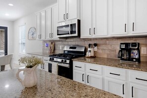A modern kitchen with white cabinets, a stainless steel stove, a microwave, and a coffee maker. - The Grand Sunnyview Home: Pool & Hot Tub / Movie Room (Houston)