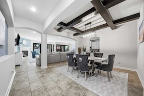 A spacious living area with a dining table, chairs, and a kitchen in the background. - The Grand Sunnyview Home: Pool & Jacuzzi / Movie Theater (Houston)