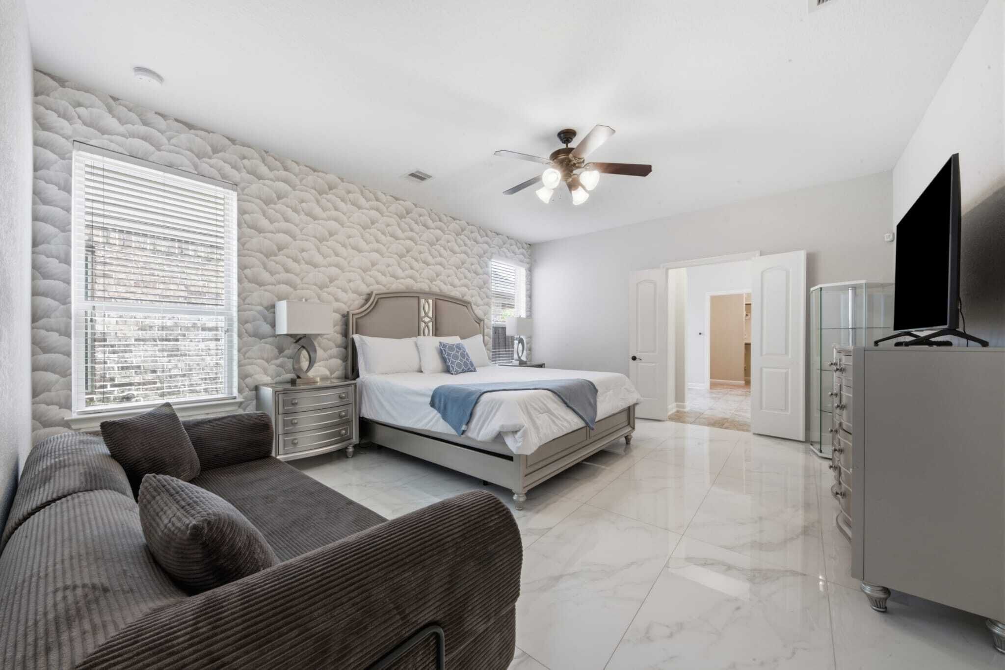 A bedroom with a bed, a nightstand, a lamp, a ceiling fan, a TV, and a wardrobe.