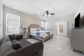 A bedroom with a bed, a nightstand, a lamp, a ceiling fan, a TV, and a wardrobe.