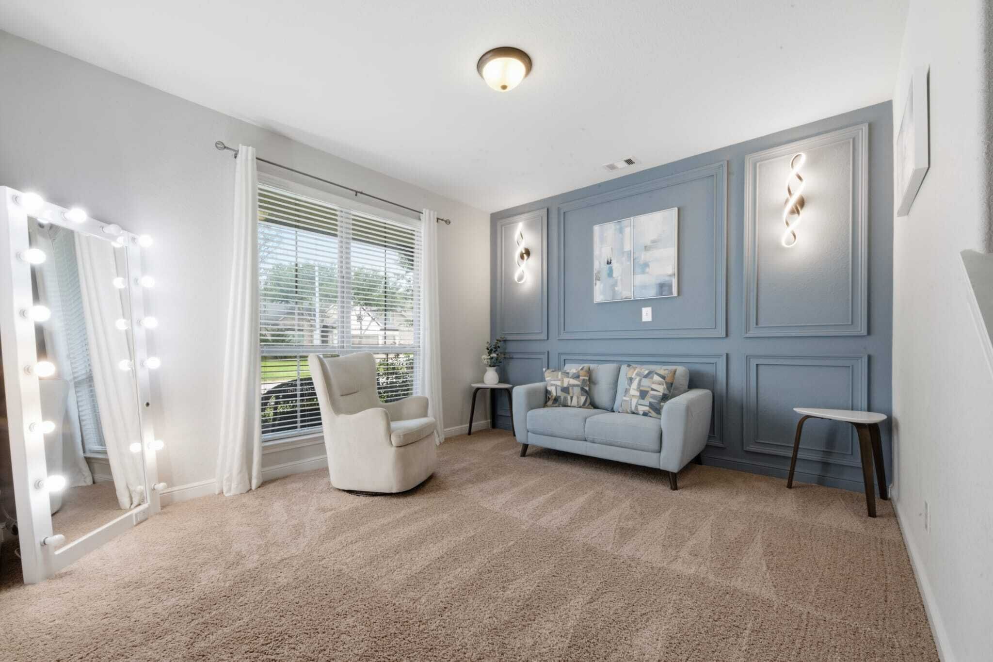 A room with a vanity mirror, a lighted wall, a sofa, and a chair.