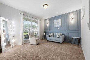 A room with a vanity mirror, a lighted wall, a sofa, and a chair.
