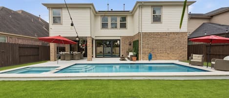 A two-story house with a swimming pool, outdoor furniture, and a brick exterior.