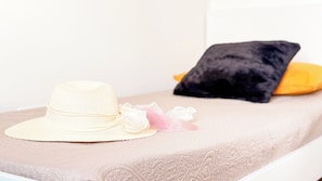 Een bed met een beige sprei, een witte hoed en een zwart kussen.