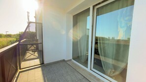Een balkon met een metalen hekwerk, een glazen deur en uitzicht op een landschap.