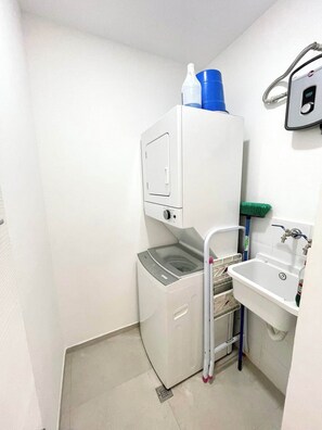 A compact bathroom with a washing machine, a sink, and a shower area. - Oceanfront 2BDR Penthouse with Jacuzzi at Playa Nueva Romana (San Pedro de Macorís)