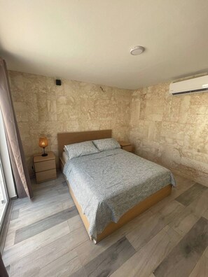 A bedroom with a bed, a nightstand, a lamp, and an air conditioning unit. - Oceanfront 2BDR Penthouse with Jacuzzi at Playa Nueva Romana (San Pedro de Macorís)