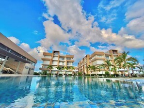 A hotel with a swimming pool, multiple balconies, and palm trees. - Oceanfront 2BDR Penthouse with Jacuzzi at Playa Nueva Romana (San Pedro de Macorís)