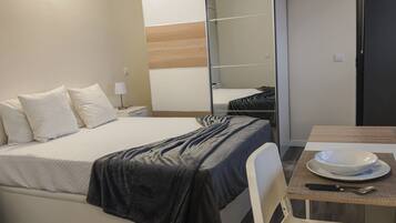A hotel room with a bed, a desk with a chair, a mirror, and a wardrobe.