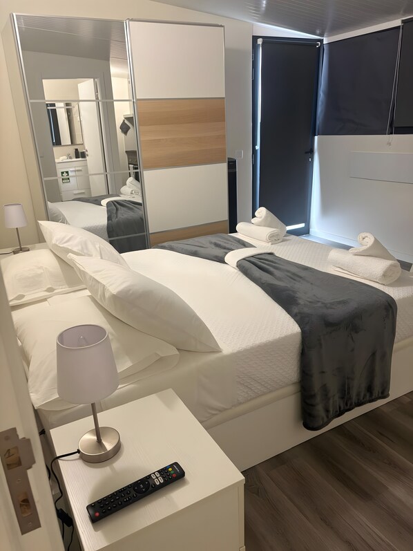 A hotel room with two beds, a bedside table with a lamp, a remote control, and a large mirror.