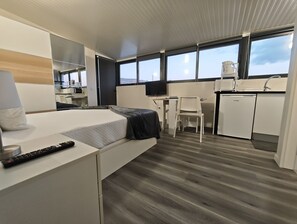 A modern hotel room with a bed, desk, chair, and kitchenette.