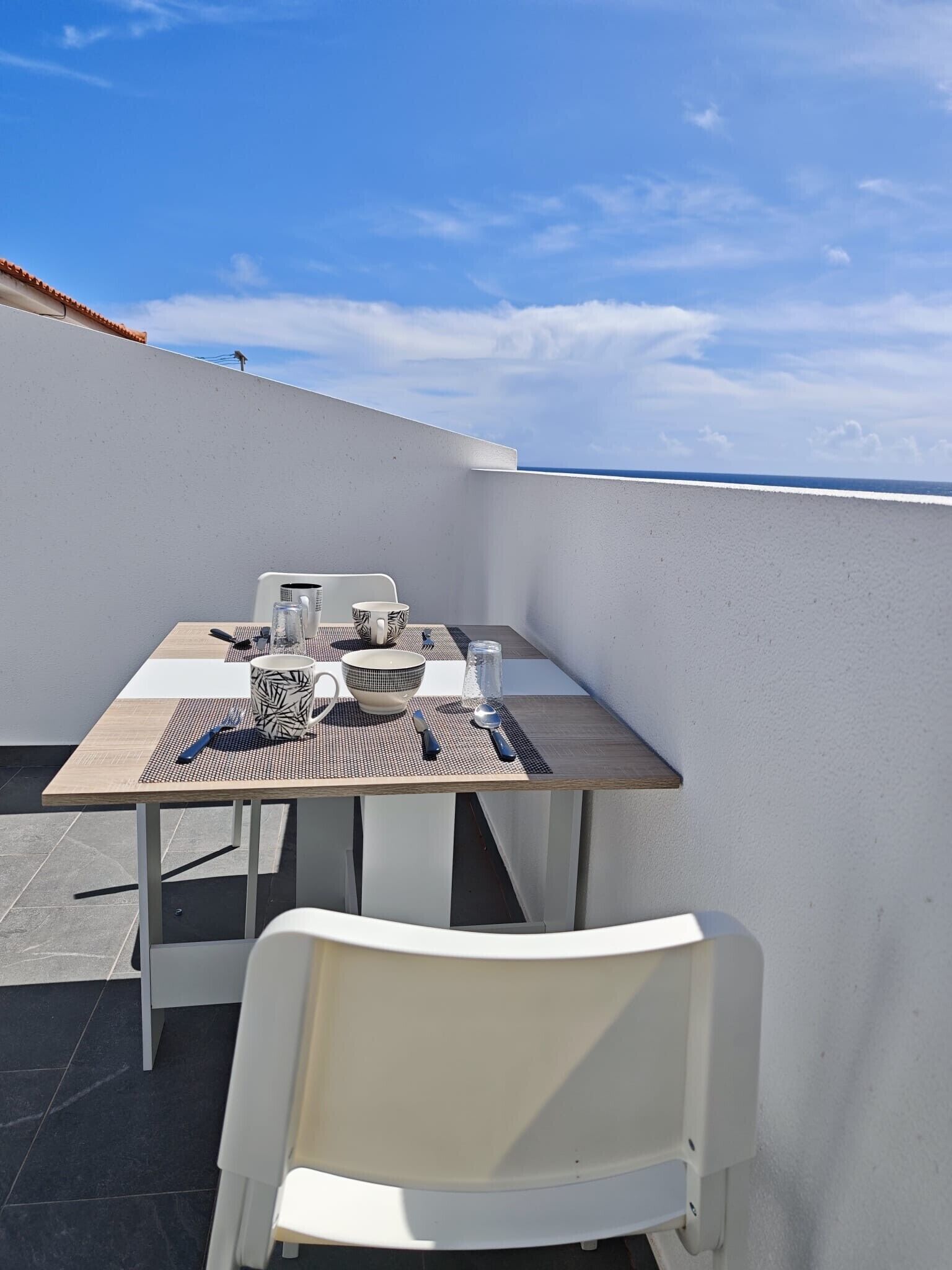 Una mesa de comedor con sillas en una terraza en la azotea, con vista despejada al cielo y al océano.