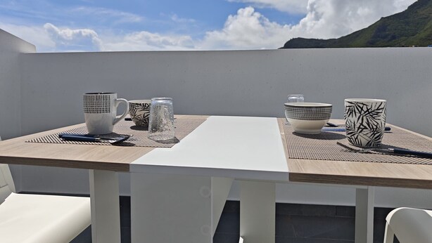A dining table with a white tablecloth, two white chairs, and a view of the sky and mountains in the background.
