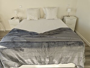 A bed with a grey blanket, two bedside tables with lamps, and a white headboard.