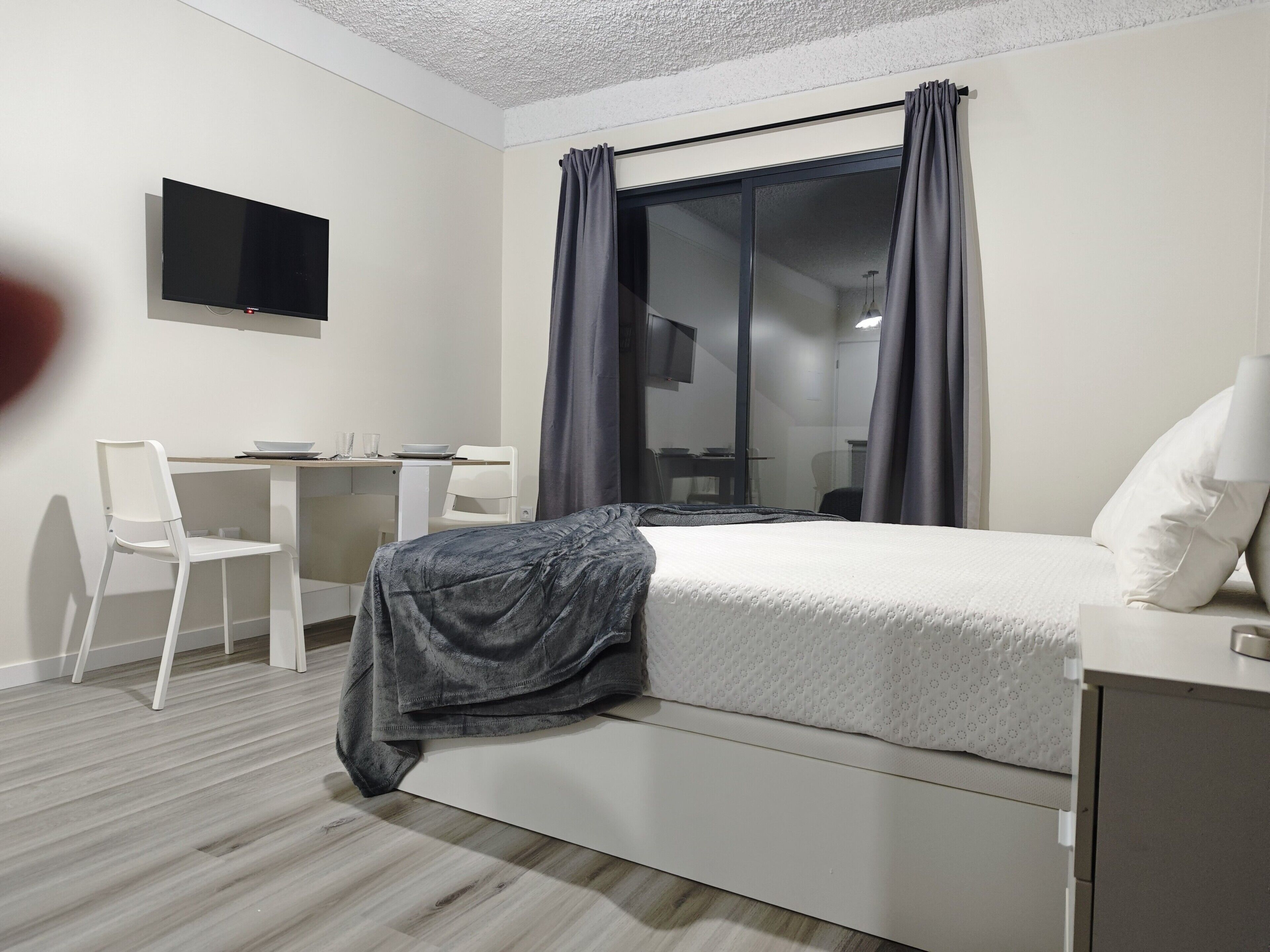 A modern hotel room with a bed, a desk, and a chair.