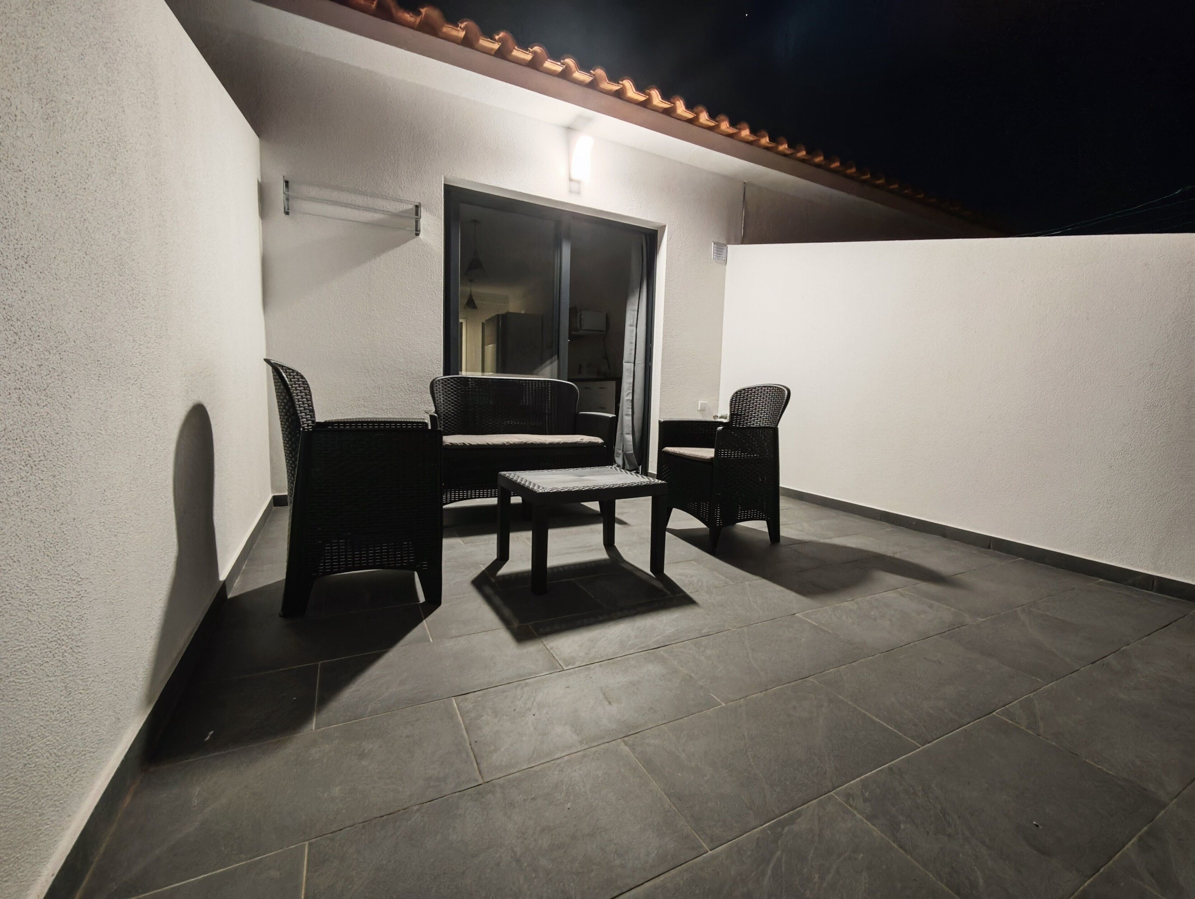 A balcony with a seating area, including two chairs and a table, and a door leading to an interior space.