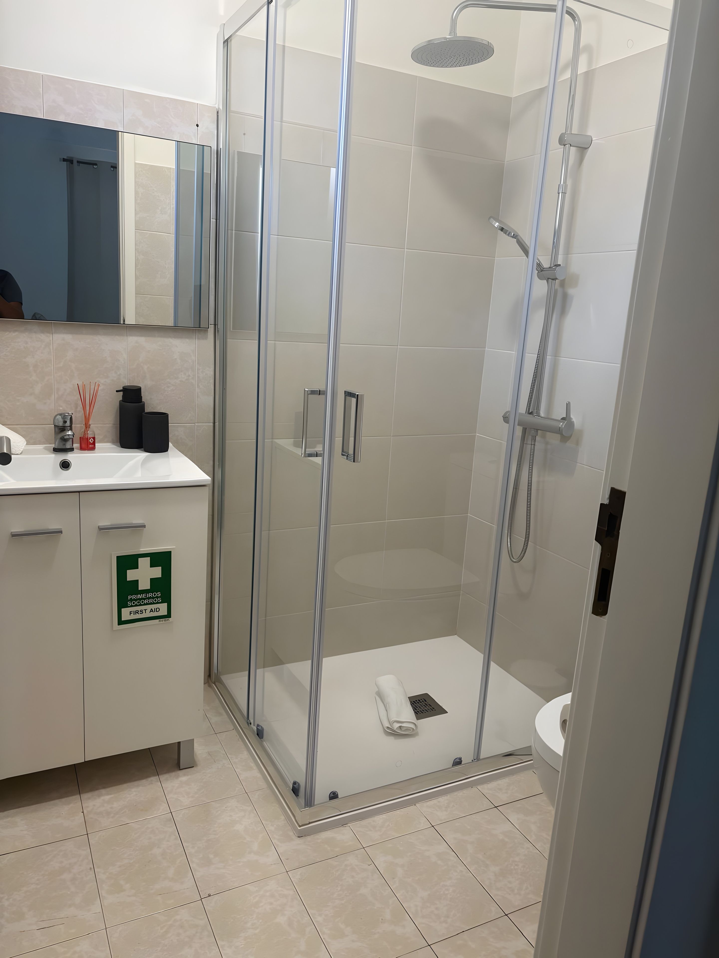 A modern bathroom with a glass-enclosed shower, a sink with a mirror above, and a sign indicating first aid availability.
