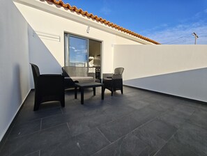 A balcony with two wicker chairs and a small table, a sliding glass door leading to an interior space, and a solar panel on the roof.