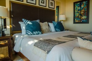 Un lit bien fait, avec une couvre-lit à motifs et des oreillers, une table de chevet avec une lampe, et un tableau accroché au mur.