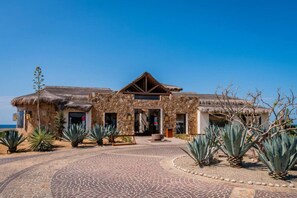 A stone building with a thatched roof, a paved entrance, and agave plants in the foreground. - Quivira Luxury Penthouse | Ocean Views & Resort Amenities (Cabo San Lucas)