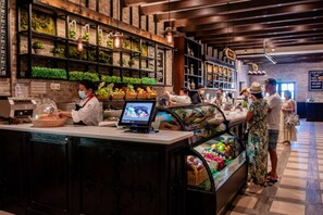 A bakery counter with a digital menu display, a fruit display case, and a person preparing food. - Quivira Luxury Penthouse | Ocean Views & Resort Amenities (Cabo San Lucas)