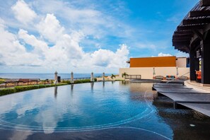 Une piscine avec vue sur l’océan, un espace salon couvert et un bâtiment à la façade orange.