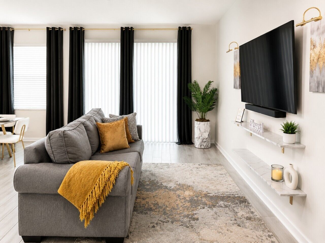 A modern living room with a grey sofa, black curtains, a flat-screen TV, and a marble fireplace.