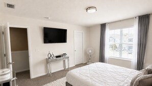 Ein Schlafzimmer mit Bett, Fernseher, Schreibtisch und einem Fenster mit Vorhängen.